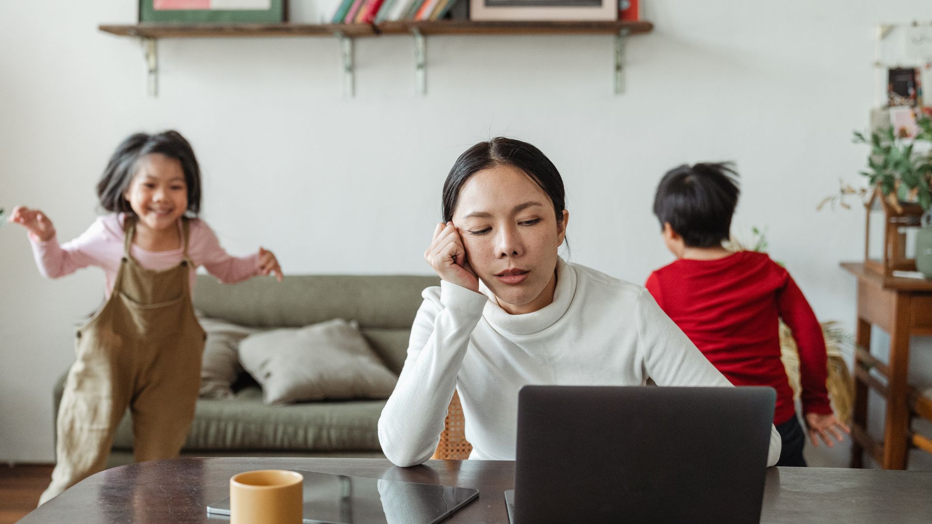 stressed mom working on laptop while kids run around